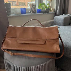 Väska från Zanellato - Jättefin väska från Zanellato i modellen Nina. Kamelfärgad. Har flera fack på insidan. Något skavd i yttre hörn. Kan bäras som en portfölj eller med axelbandet.   Kan skicka fler bilder om det önskas!