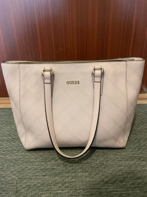 Guess rosa axelremsväska - Lagom stor väska, rosa, köpt 2018 men använd fåtal gånger. Två innerfack på vardera sida, ena med dragkedja.  Dustbag medföljer