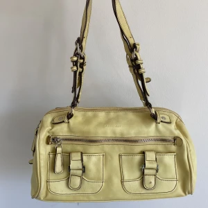 Ljusgul handväska med justerbara band - Somrig gul handväska med svarta kontrasterande sömmar, silverdetaljer och justerbara band. Bredd (längst ned): 11, längd (längst ned): 31, djup: 19, band: 53 (kan göras 18 cm längre)🍰🌞💛 Några små fläckar samt saknar ett litet läderband, fråga efter bild!