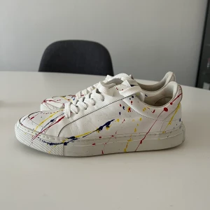 Difficult by P: Madison Picasso Ltd Edit - Säljer nu dess unika och magiska skor från Difficult by P. Dessa sneakers är unika och tillverkade i begränsade upplagor om max 100 par.   Modell: Limited Edition, Madison Storlek: 37  Sneakersna är handsydda och kantsydda i Italien från en familj som har gjort detta i generationer. Dessa sneakers är gjorda av mjukt kalvskinn med en vit färg och en handgjord stänk av rött, gult och blått.  Använda ett fåtal gånger i hopp om att det ska passa mig… tyvärr är det snäppet för stora för mig :(  