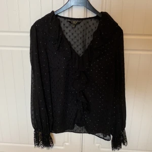 Blus från Lipsy London  - Fin svart blus med skimmriga prickar från Lipsy London. Nyskick använd ett fåtal gånger. Köpt i London för 700 kr. 