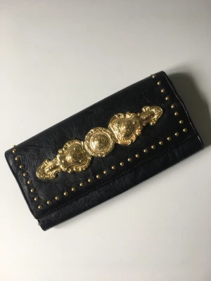 Svart kuvertväska med gulddetaljer - Svart kuvertväska i läderimitation. Stora gulddetaljer.  Fint skick bortsett från lite skav (se bild).  
