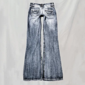 Lågmidjade jeans - Midja 75 innerben:84 Jeans med detaljerade bakfickor. Lowwaist bootcut. Slitningarna skulle jag tro är del av designen. Ytterst svag fläck vid ena fotändan, kan eventuellt gå bort I tvätt. Smått nötta vid fickor och fotändar men överlag fint skick🤍