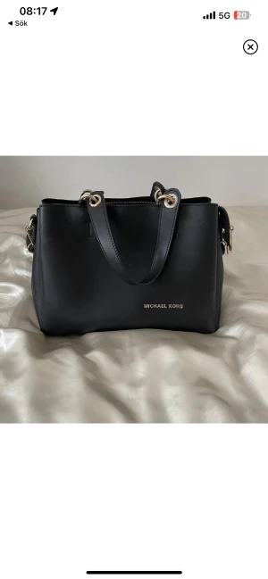 Michael skors väska - Supersnygg och modern Michael kors väska med matchande plånbok ( glömde ta med den här, kan skicka bild vid önskan ). Väska har även en lång band som kan sättas på och av som ni ser på bild. Helt perfekt  med fickor och plats!