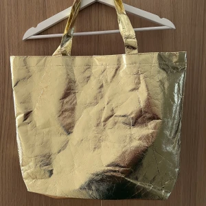 Underbar tygväska i guld! - Stor och rymlig tygväska i glänsande guld, går att stänga med dolda kardborreband i mitten. Knappt använd. Bra kvalité!