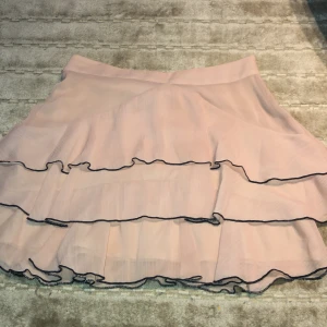 Somrig beige kjol  - Cool rosa/beige kjol från zara, kort och har svart kant på volanger💕 i Bra skick. Fin till sommaren eller hösten med strumpbyxor, lite liten i storlek så funkar på XS och S