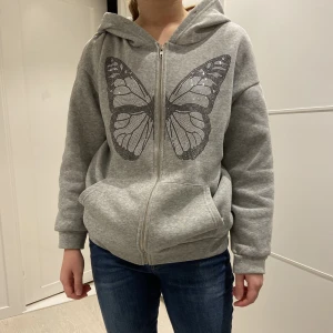Grå ziphoodie  - En grå lite oversized zip-hoodie med en strassad fjäril! Skön och snygg! Knappt använd. Saknar snören