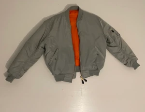 Bomberjacka - Silvergrå vändbar bomberjacka i storlek M-L. Orange insida