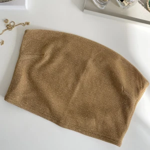 Glittrig tubtopp H&M - Guldglittrande tubtopp från H&M. Köpt förra sommaren men är aldrig använd!