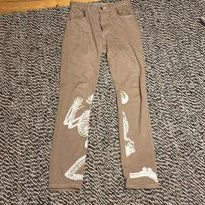 By slik - Biegea jeans med med ett skelett på knä och döskallar på fickorna. Stl. Regular 28.  Stretchiga och sköna 300kr eller byte