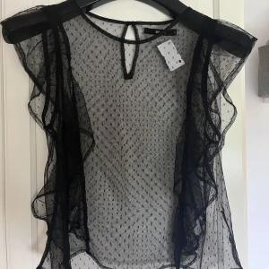 Genomskinlig topp med spets! - Supersnygg svart spetstopp med volanger och prickigt mönster! Perfekt att ha över ett svart linne eller BH.   Säljer då jag har andra liknande och denna inte kommer till användning.