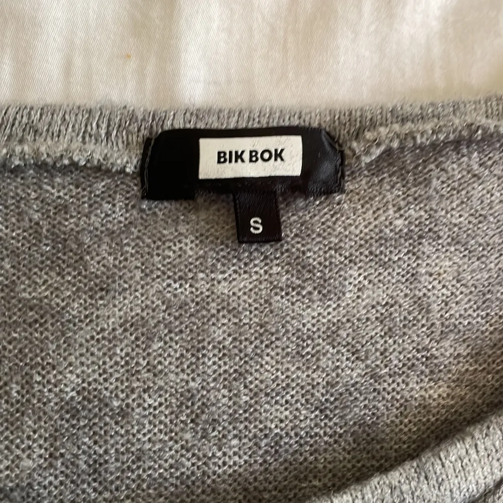 Det är en stickad tröja med en dödskalle på den är grå och den har svarta paljetter på . Toppar.