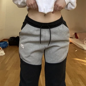 Nike tech byxor  - Nike tech byxor för både män och kvinna. Grå/svart Bra skick men ett litet ihop sytt hål vid benet så syns knappt. Köpare står för frakten