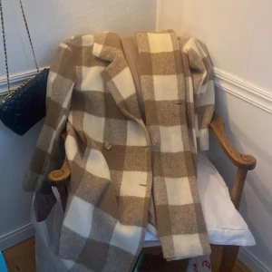 Kappa - Rutig kappa från ginatrico. Går ner till knäna och har en slits i bak. har knappar långt med hela framsidan. 