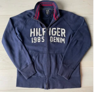 Tommy Hilfiger-kofta  - Stilren, unik och bekväm Tommy Hilfiger-kofta (med zip) säljes! Tröjan är i använt skick men har inga defekter såsom hål, fläckar eller missfärgningar. Frakt ingår i priset! 