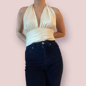 Krämfärgad halterneck topp - Marilyn Monroe inspirerad halterneck topp i storlek XS. Jag är XS men detta plagg var för liten för mig då jag ej kunde knäppa knapparna på baksidan och därav ej kunnat använda den. Synd för det är en jätte snygg topp från bik! (100% Recycled Polyester) 