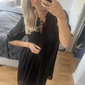 Klänning  - Fin klänning med detaljer i tyget och knyte vid halsringning och ärmar