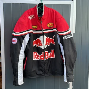 Red bull jacka - Jackan är i tyg, med märken i skinn eller liknande materil.  Innerjacka borttagbar, ryggskydd, armskydd, axelskydd.  Storlek 3xl, själv brukar jag ha xl men denna passar perfekt. Vintage