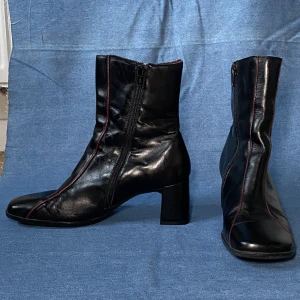 Skinnstövlar med röd rand - Snygga stövlar från Air Sweet i äkta läder med bred platt klack. Köpta second hand så slitage enligt minst två personers flitiga användning. Men väldigt välbevarad utsida trots detta.