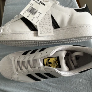 Superstar Adidas skor - Köpte skorna till mitt ex innan vi gjorde slut. De är inte i min storlek så säljer dem. Helt nya, aldrig använda utomhus endast provade av två personer. Lådan har varit med om en flytt så är ganska mosad.   Nypris: 1 145kr 