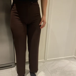 Bruna kostymbyxor - Säljer mina ursnygga bruna kostymbyxor för ett superbra pris då de tyvärr blivit för tajta på mig. Använt ett fåtal gånger och har en extra knapp till! Passar perfekt året om och är så eleganta! Hör av dig vid intresse och för mer info🧸🕰️🥥