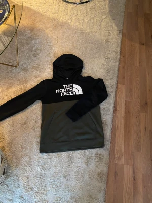 The North Face Huvtröja Xl Barn - En nästan oanvänd The North Face huvtröja som har färgen grön och svart Den har ett väldigt skönt material och funkar till nästan alla tillfällen Strl XL Barn men funkar för män eller tjejer i xs och i vissa tillfällen s Den är nästan helt oanvänd.