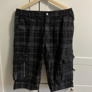 Alternativa rutiga cargoshorts - Jättefina långa shorts i alternativ stil med cargofickor dekorativa dragkedjor, storlek M, köpt på EMP shop, i väldigt fina skick, nästan helt oanvända