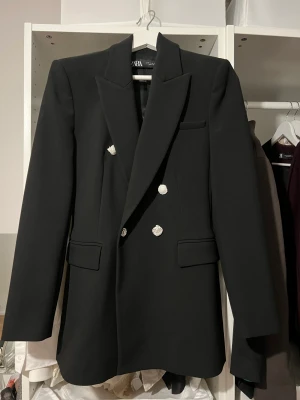 Svart Blazer  - Strukturerad blazer från ZARA med axelvaddar. Mycket bra kvalité, enda defekt på varan är däremot att en knapp har lossnat och hittar tyvärr inte den. OANVÄND. Nypris cirka 899kr