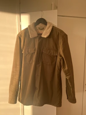 Olivgrön overcoat - Måttligt använd och slitstark overcoat från Levi’s med teddy-interiör! Sval på sommaren, varm på höst/vinter. Säljes då jag växt ur den