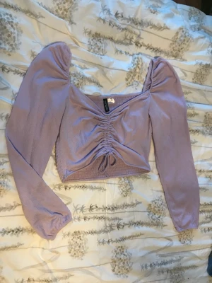 Lila top - En ljus lila top med dragsko i mitt fram och puffärm från HM i storlek M. Den är i gott skick och har endast använts några få ggr☺️