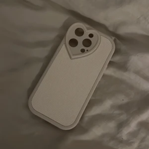 Vitt mobilskal med hjärta - iPhone 14 pro - Oanvänt mobilskal till iPhone 14 PRO. Fint vitt skal med hjärta runt kameran. Silikon-aktigt material.