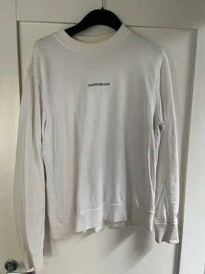 Calvin Klein jeans tröja - Snygg vit Calvin Klein jeans tröja i strl L som är använd enbart ett fåtal gånger. I mycket bra skick utan fläckar.
