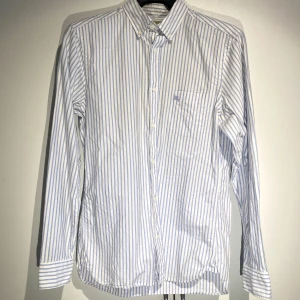 Burberry skjorta Blårandig Oanvänd - Hej, säljer en väldigt elegant och stilren skjorta från Burberry. Nypris 5000kr. Grym kvalite, perfekt under en ziptröja, kavaj eller bara med ett par jeans. Perfekt skick, oanvänd. Strl small och True To Size. Pris kan diskuteras. Hör av dig vid frågor. 