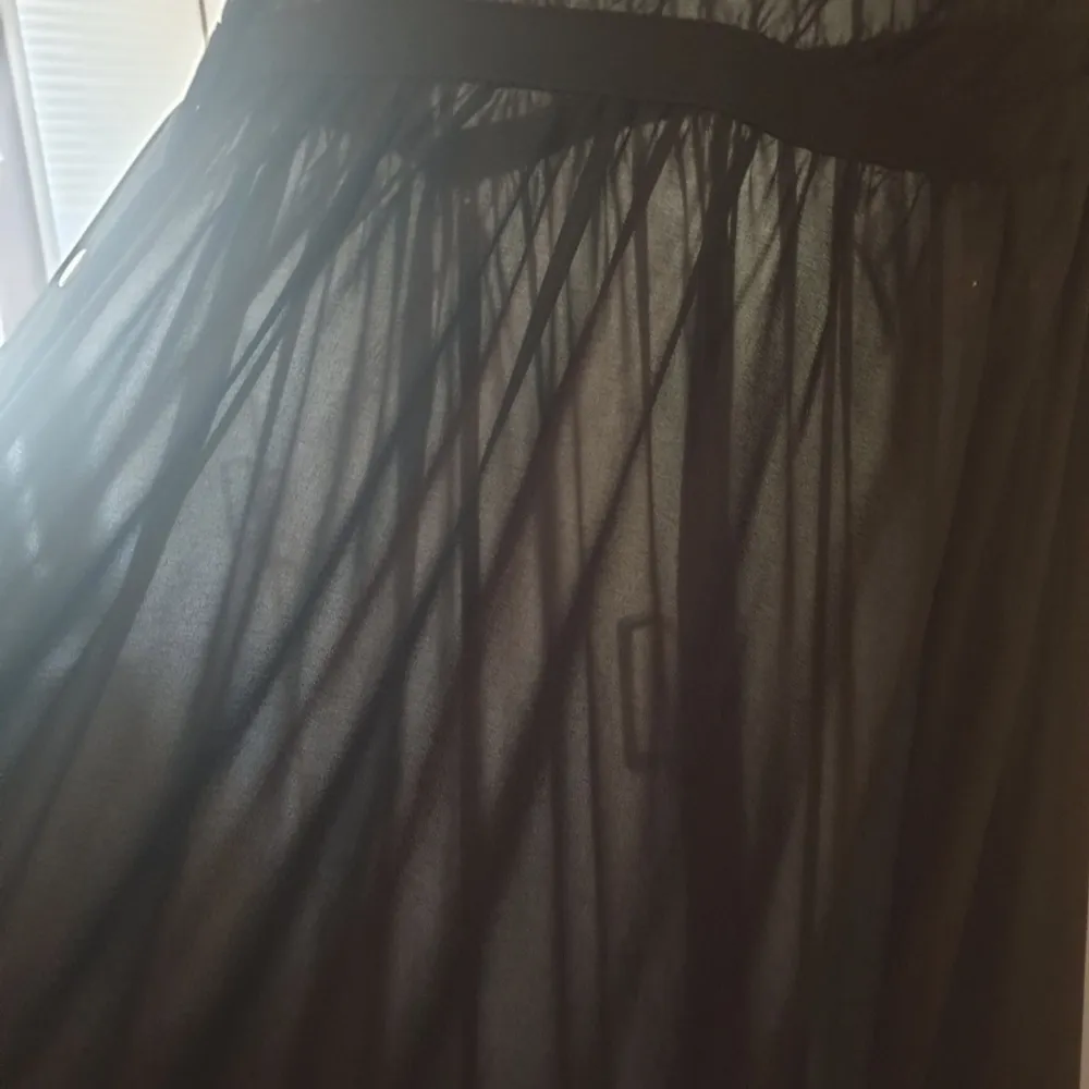 En svart, genomskinlig klänning från Glassons. Bröstfickor och bronsfärgade tryckknappar. Resår i midjan, kjollängd från resåren: 100cm. 100% polyester. . Klänningar.
