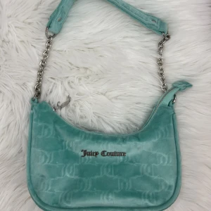 Juicy couture väska - Så fin juicy couture väska som jag köpte på urban outfitters i Stockholm. Har knappt använd den och ser ut som ny. Den är i sammets tyg och typ en grön blå färg med juicy tryck över sig samt loggan. Rymmer mer än vad man kan tro faktiskt!