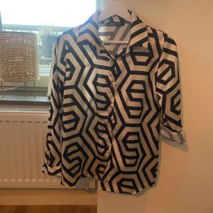 Mönstrad skjorta i silke.  - Mönstrad skjorta i silke. Beige/gräddvit/svart/guld.   Använd 1 gång. Stor i storleken! 