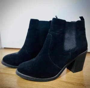 Svarta ankelboots av mocka, strl 41, säljes i nyskick, aldrig använda. - Boots med resår vid ankeln vilket ger skorna en elastisk passform. Klack ca 8 cm (mätt vid hälen),  bekväma att gå i.  Liten strl 41, passar även normalstor strl 40. Skorna är impregnerade. Nypris 499 kr  Säljes för 89 kr. 