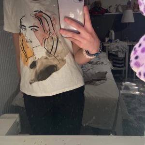 Vanlig t-shirt med ett ansikte på  - Det är en vit tröja med en design av ett ansikte och samt färger på ansiktet. Den är jätteskön och jättefin och den har ett litet hål som knappt syns över vänstra axeln men annars är den i jätte bra skick 