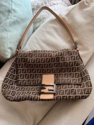 Jättefin Fendi Baguette väska - Säljer min Fendi väska, mama baguette, inköpt 2021 på Vestiaire Collective. Jättefint skick både utvändigt och invändigt, utan skråmor och fläckar.  Lite repor på själva Fendi spännet men inget man tänker på.  Kvitto finns!