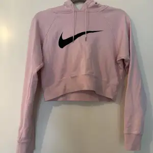 Ljusrosa croppad hoodie från Nike, logga både fram och på luvan. Bild 1 & 2 visar rätt färg bäst. Bra skick 
