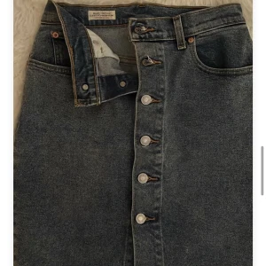 Kjol från Levis  - Kjol från Levis. Slutar en bit ovanför knäna beroende på hur lång man är men kjolen i sig är lite längre. Knappar hela vägen framtill. Storlek 26
