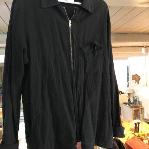 Svart Overshirt från L’Homme Rouge, med dragkejda, fickor och bröstficka. 50% Linne, 50% Bomull. Sparsamt använd och i gott skick.  