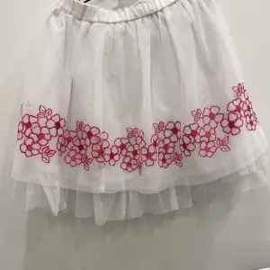 En vit kjol av tyll med rosa blommor längs kanterna. En väldigt fin kjol som kan användas vid olika tillfällen.