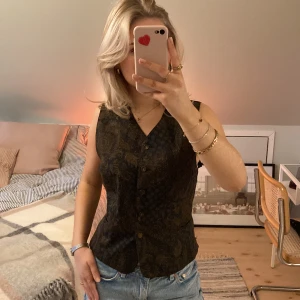 Kostymväst  - Skitsnygg och unik kostymväst (vintage). Paisley mönster i svart och vinrött. Knappt använd av mig. Snygg att ha knäppt som på bilderna eller uppknäppt över en långärmad tröja. Knytning i ryggen, därav kan storleken varierar. Jag har knutit den längst in.