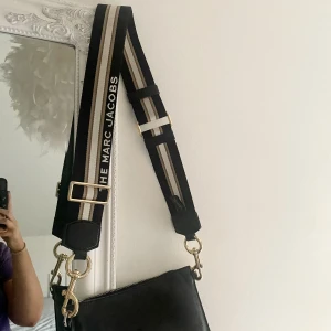 Marc Jacobs väskband - Säljer mitt väskband från Marc Jacobs. Det har i stort sett inga tecken på användning, det är justerbart och hur fint som helst. Man kan sätta på bandet på vilken önskad väska som helst, på bilden har jag det till en svart från Carin Wester🤗