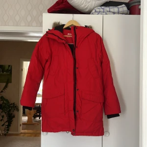 Jacka  - Snygg & varm ny röd Everest vinter jacka.  Har en ficka på insidan samt fyra fickor på utsidan & luva med päls.  Finns både dragkedja & knappar. Storlek 34.