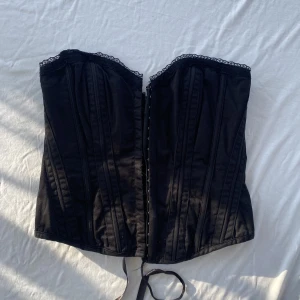 Korsett svart  - Svart korsett från BAY. Knäpps fram med hakar och kan justeras bak med band. Kan bäras med eller utan band. Har spetsdetaljer. Storlek 10, motsvarar ca M. Köps via Swish eller köp nu 💋