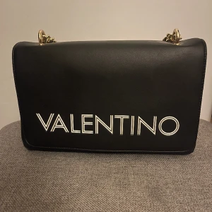 Valentino vätska - En valentino handväska. En bred på 25 cm och en höjd på 16 cm. Använt den en gång. Fick den i födelsedagspresent för två år sedan och har bara kommit till användning vid ett tillfälle. Väl omhändertagen. Hör av er om ytterligare frågor.