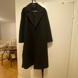 Svart lång kappa - Säljer min svarta kappa jag använt en vinter, den är i bra skick men nopprig som dem flesta blir. Den har en slits på baksidan längst ner och har ett bälte till. Två fickor finns. Skulle säga att den passar en M/L.