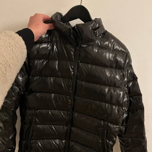 Svart glansig vinter jacka  - En kort svart glossy jacket. Super fin, i bra skick använd några få tal gånger bara så det är som att den är ny! Den är i storlek M 